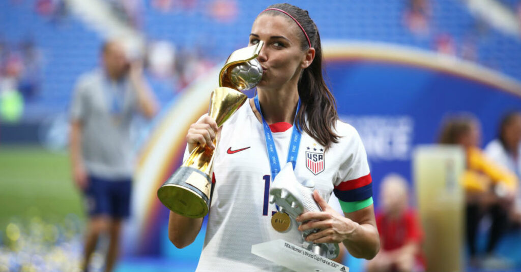 a women's football player holding and kissing her trophy